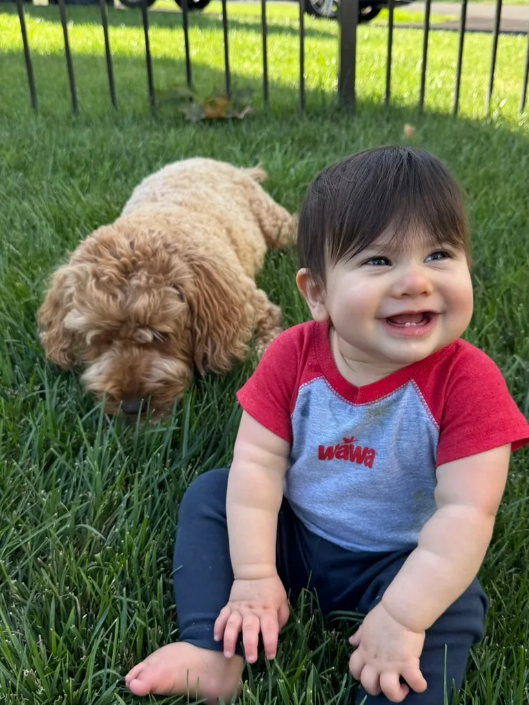 Joey Rhode sitting in the grass beside Enzo, the family goldendoodle